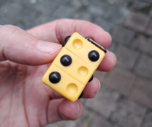 Schlüsselanhänger mit Braillepunkten, die sich drehen lassen (ähnlich wie Rubicks Cube) und mit denen man alle Braillezeichen formen kann. Auf dem Foto ist ein S gebildet.