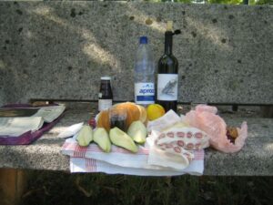 Ausgebreitetes Picknick auf einer Steinbank mit Brot, Wein, Früchten, Käse, Fleisch 
