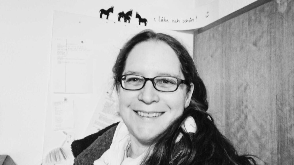 Selfie von Susanne, schwarz-weiss. Lachend, im Hintergrund Esel und der Text "s Läbe isch schön"